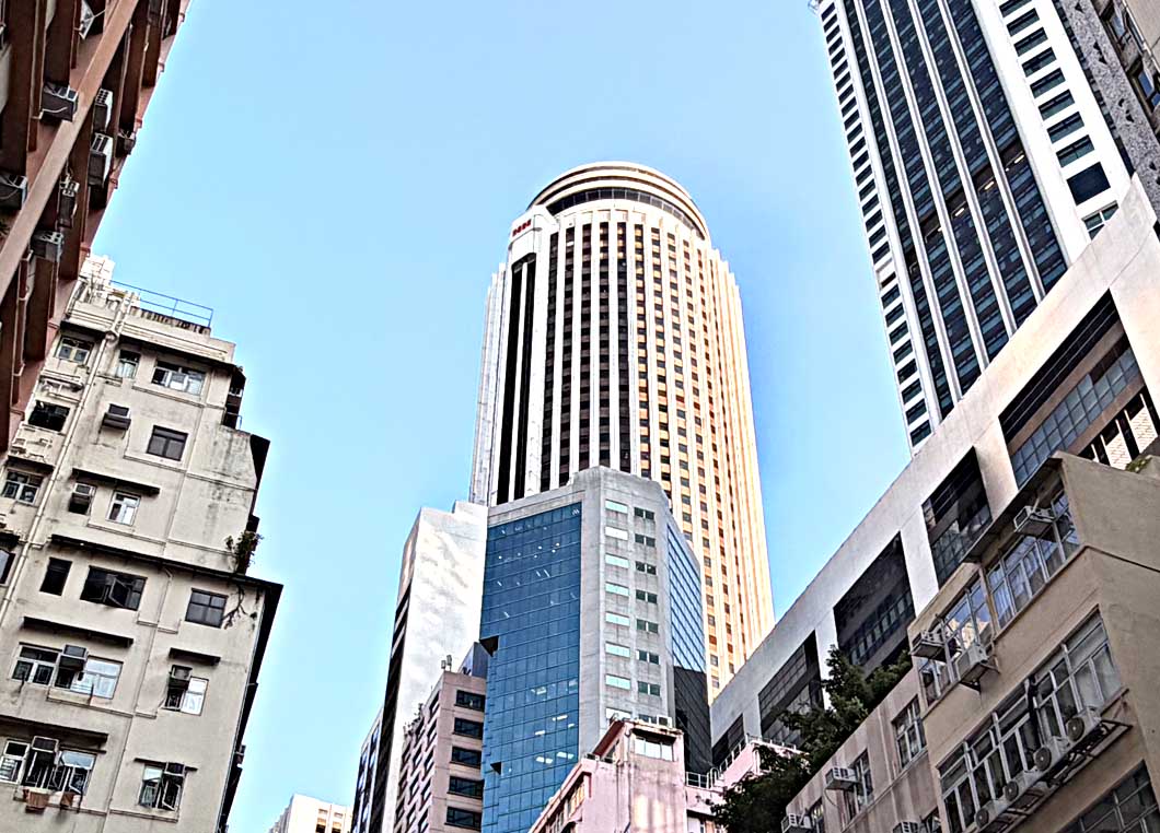 香港灣仔皇后大道東合和中心外觀，低角度仰拍1980年落成的64層圓柱形摩天大樓，藍天下可見垂直線條立面與周圍舊樓